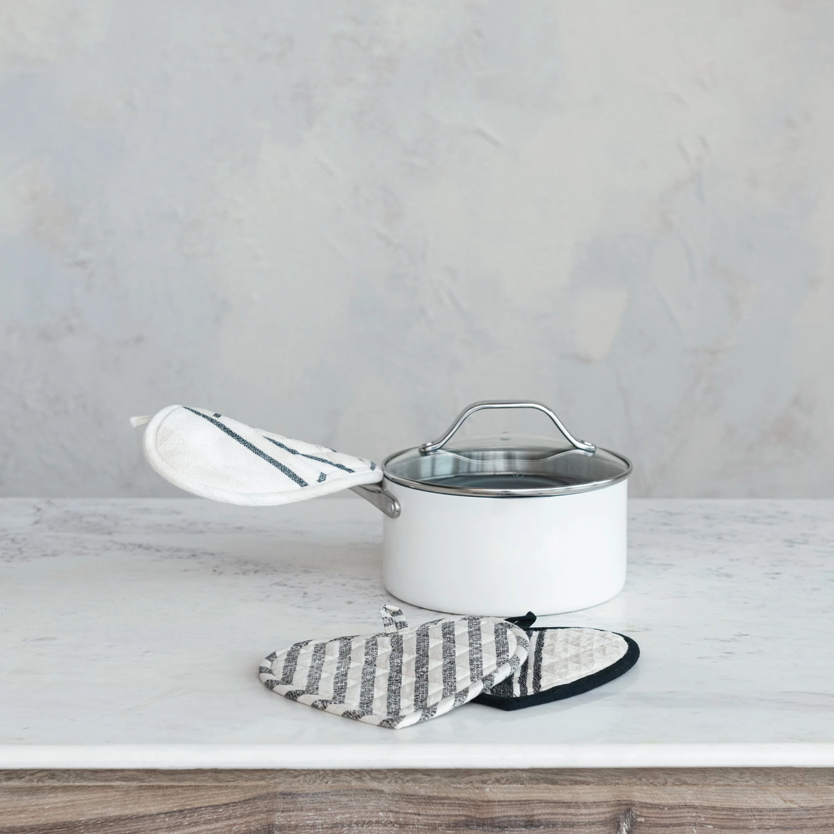 Cotton quilted heart-shaped pot holders with black and white stripes next to a white saucepan.