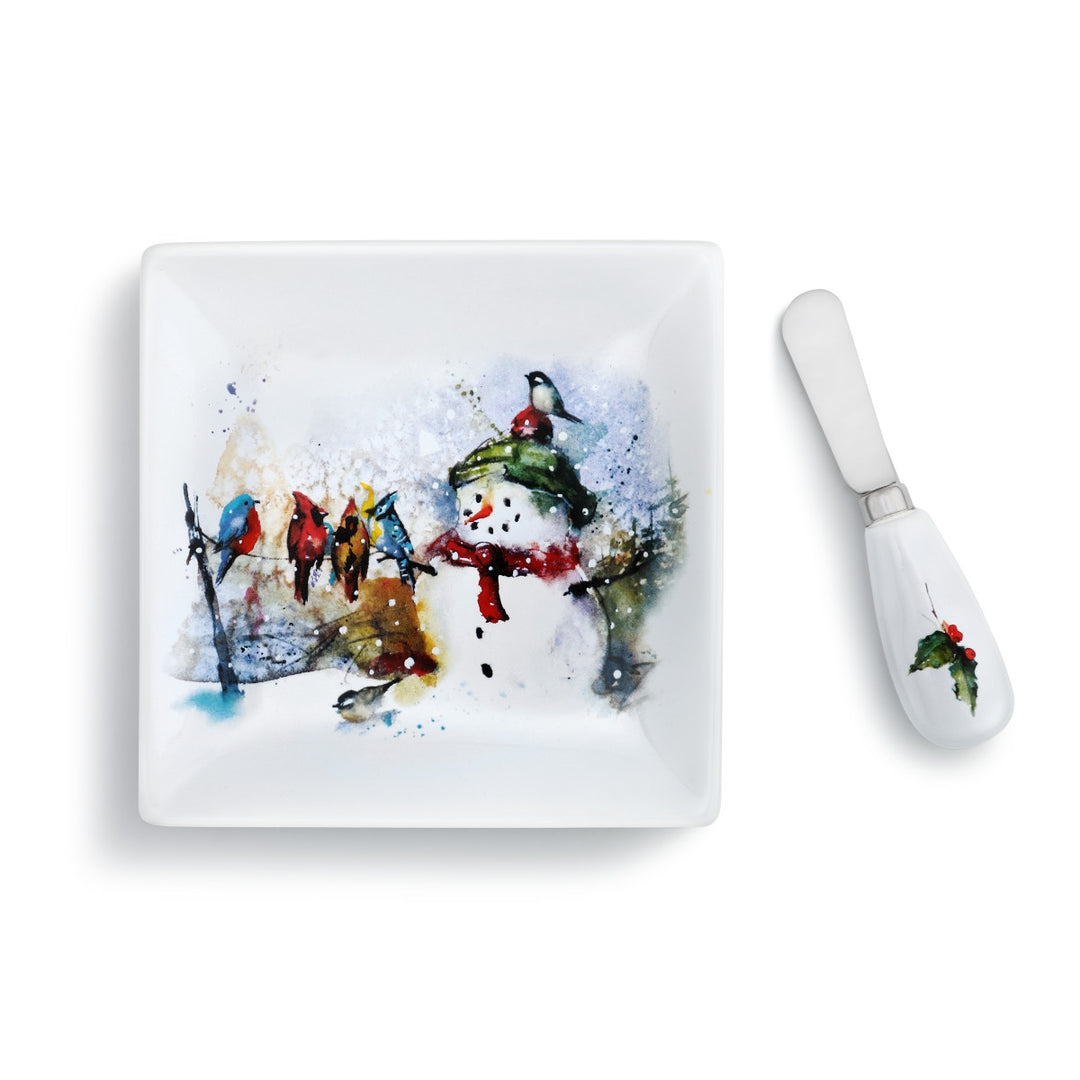 White square plate with a watercolor snowman and birds design, paired with a white spreader with a holly accent.