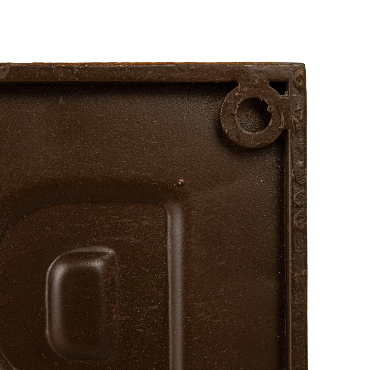 Close-up of the back corner of a brown embossed metal wall sign showing a mounting hole.