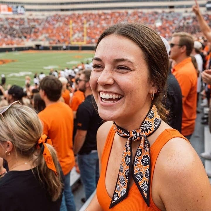Woman wearing an Oklahoma State Cowboys skinny scarf with orange and black floral patterns.