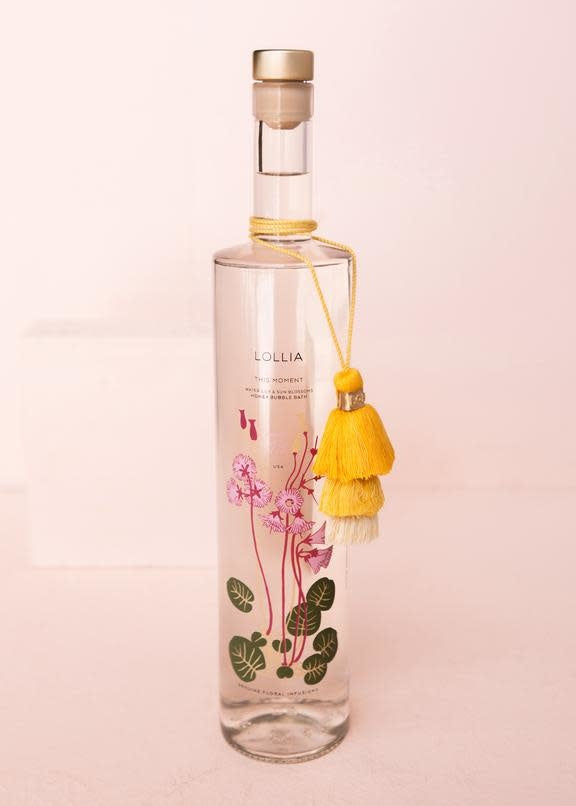 Slender glass bottle of This Moment bubble bath with tiered tassel cap.