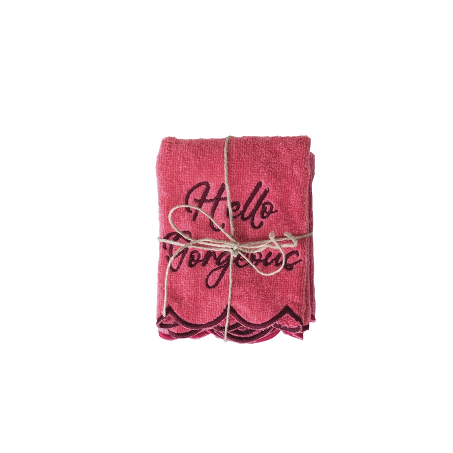 Pink square cotton washcloth with scalloped edges and 'Hello Gorgeous' embroidered in dark thread.