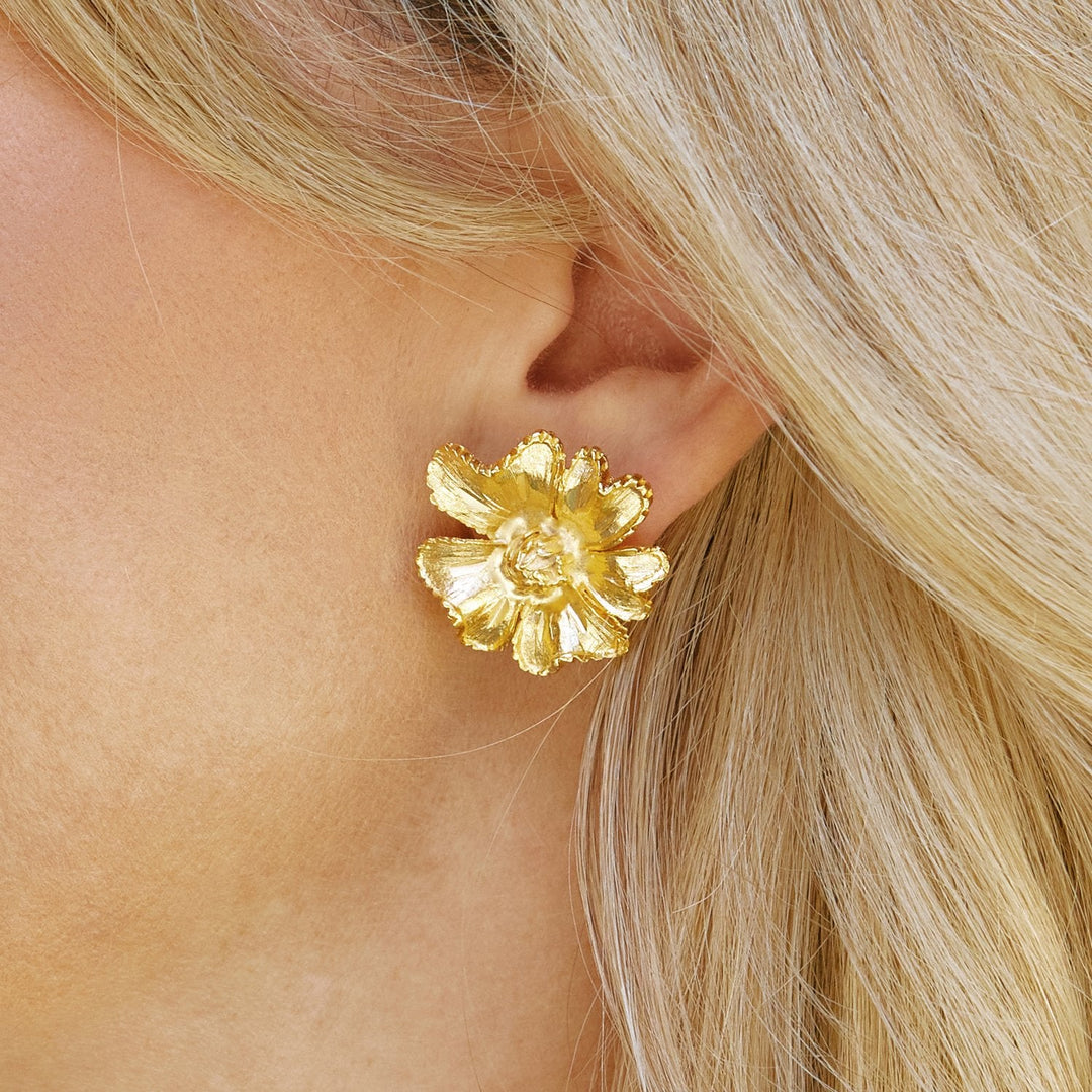 Close-up of a person wearing a gold marigold flower stud earring.