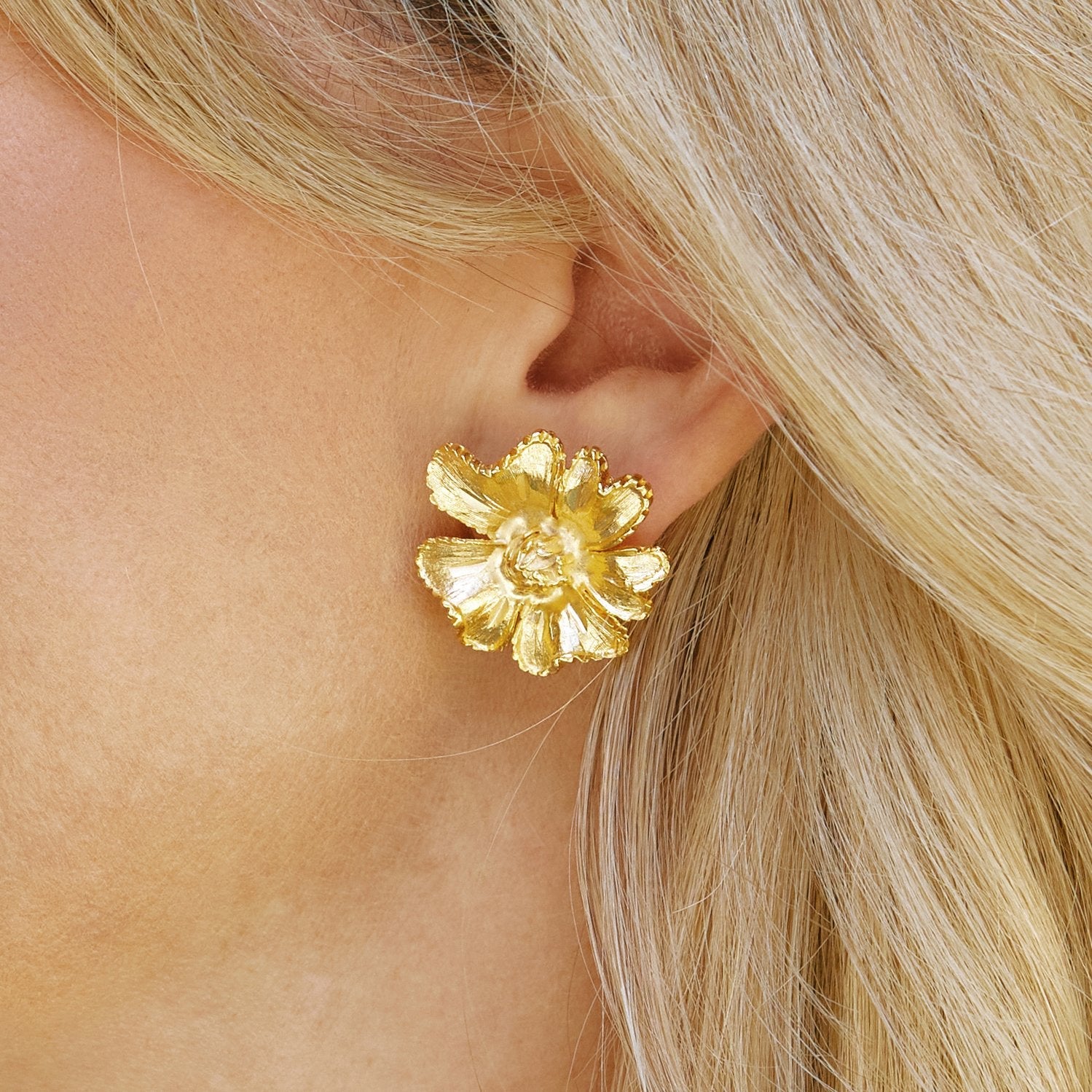 Close-up of a person wearing a gold marigold flower stud earring.
