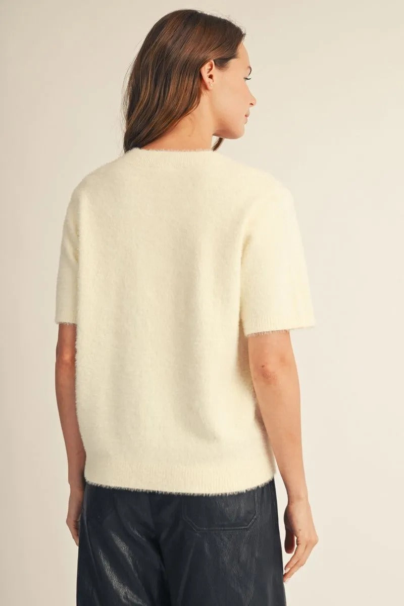 Back view of a woman wearing a cream-colored, short-sleeved fuzzy knit sweater cardigan.