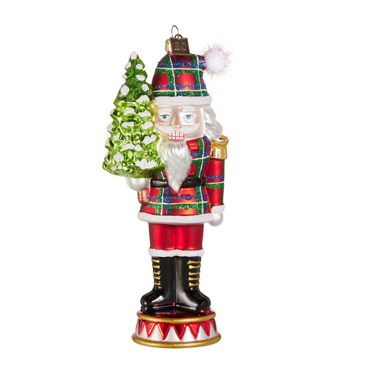 Glass and resin nutcracker ornament wearing a plaid uniform and hat, holding a small green tree.