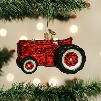 Red glass Old Farm Tractor Ornament hanging on a Christmas tree branch.