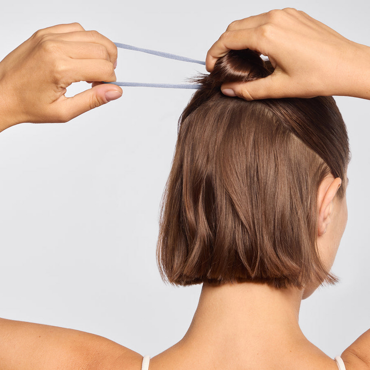 A person using a light blue seamless hair elastic to style a half-up bun on short brown hair.