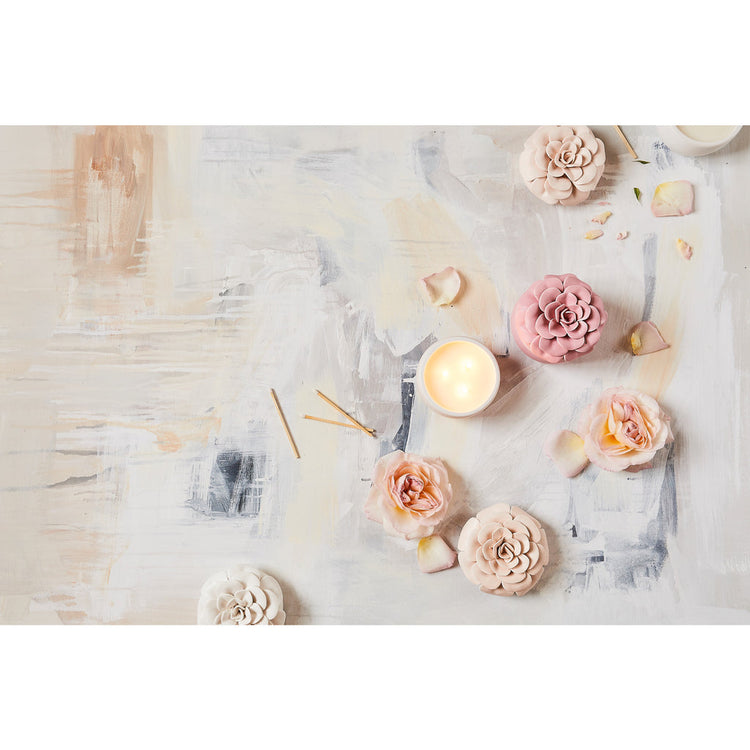 Ceramic flower candle with three wicks lit, surrounded by decorative ceramic and real roses.