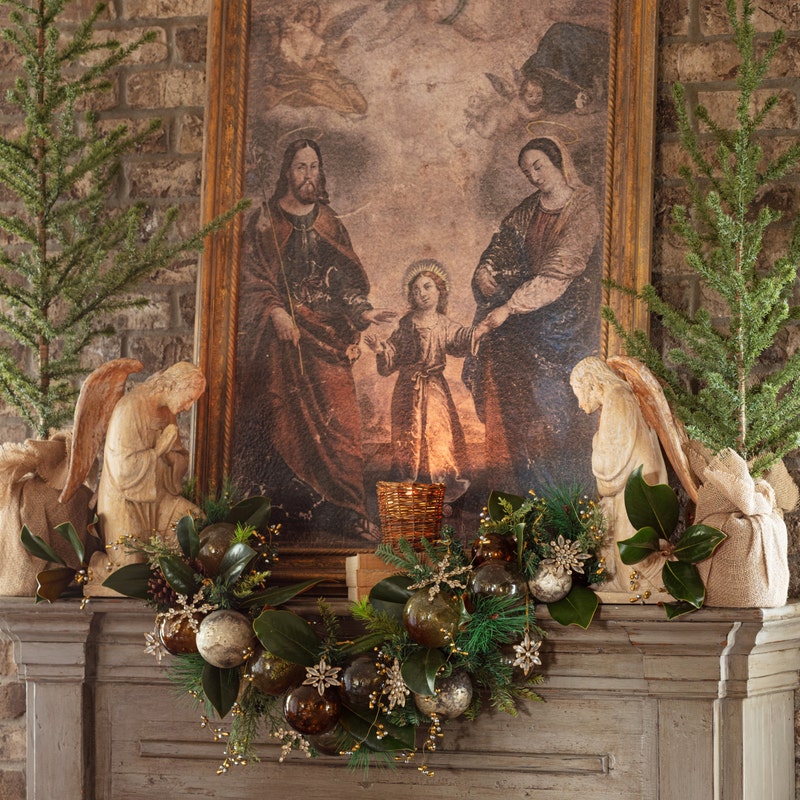 Two Herald Angel statues with a plaster wash finish flanking a religious painting on a mantel.