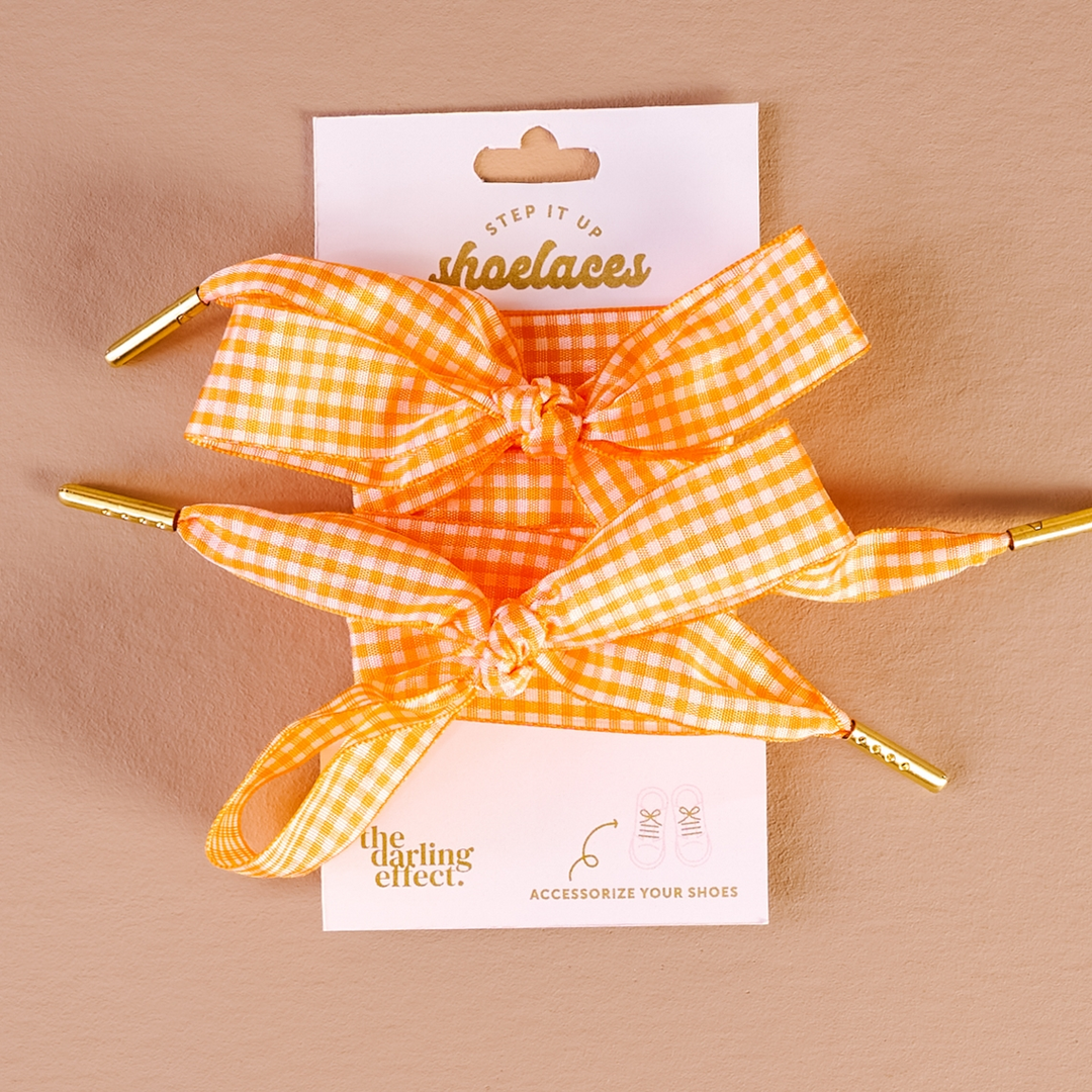 Orange and white gingham patterned shoelaces with gold metal tips on a white display card.