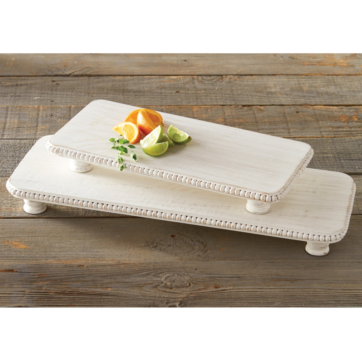 Set of two white-washed mango wood footed serving boards with beaded rims and citrus slices.
