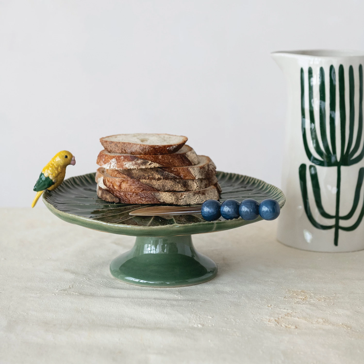 Green stoneware pedestal with yellow 3D bird sculpture on top.