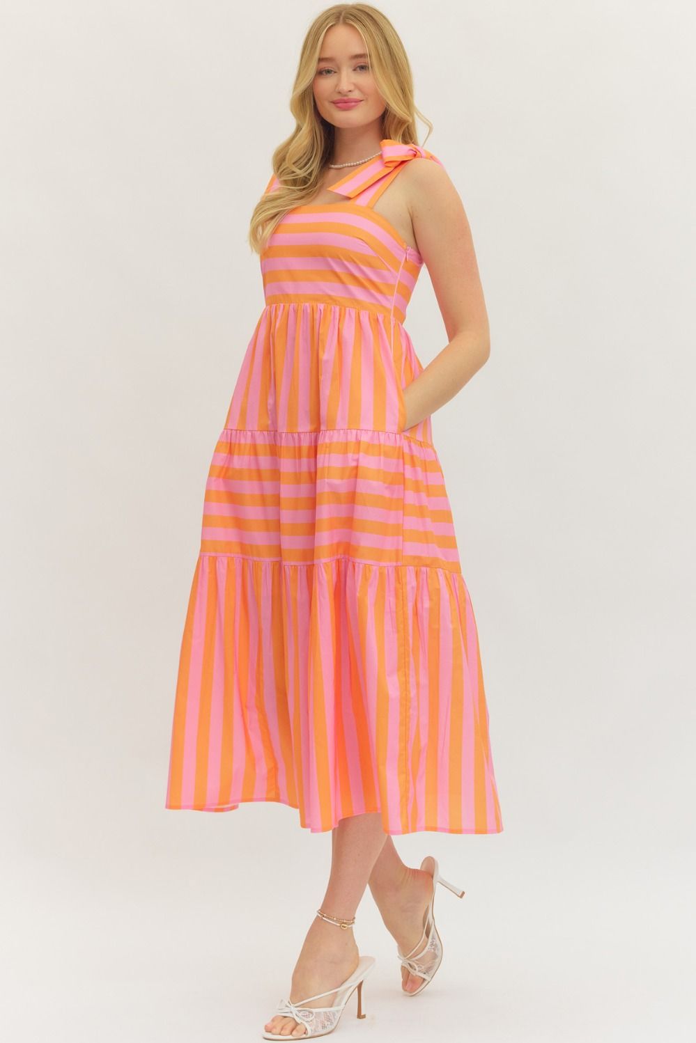 Woman wearing the Zariyah pink and orange striped sleeveless midi dress with bow shoulder straps.
