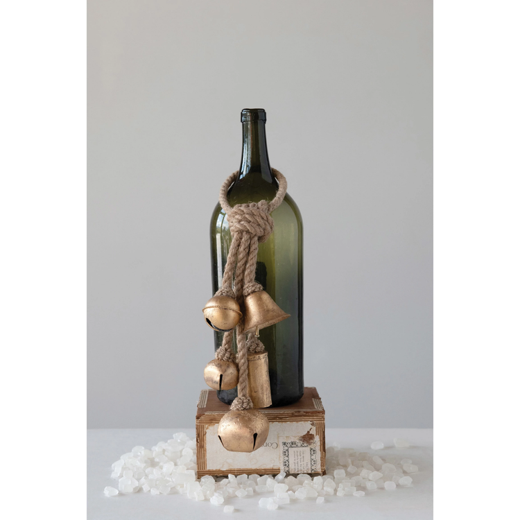 Five gold-finished decorative metal bells hanging from a thick jute rope on a green glass bottle.