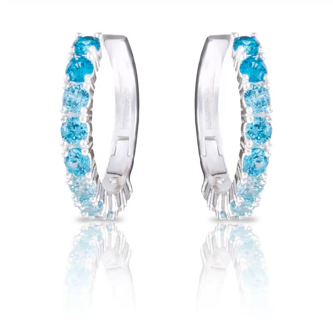 Silver huggie hoop earrings featuring a gradient of light to dark blue cubic zirconia stones.