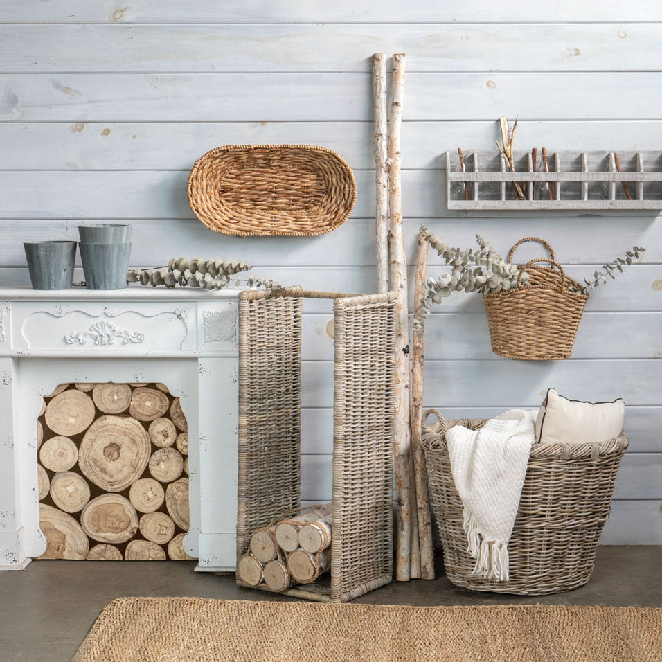 Large oval rattan storage basket with a white throw blanket and pillow in a rustic room setting.