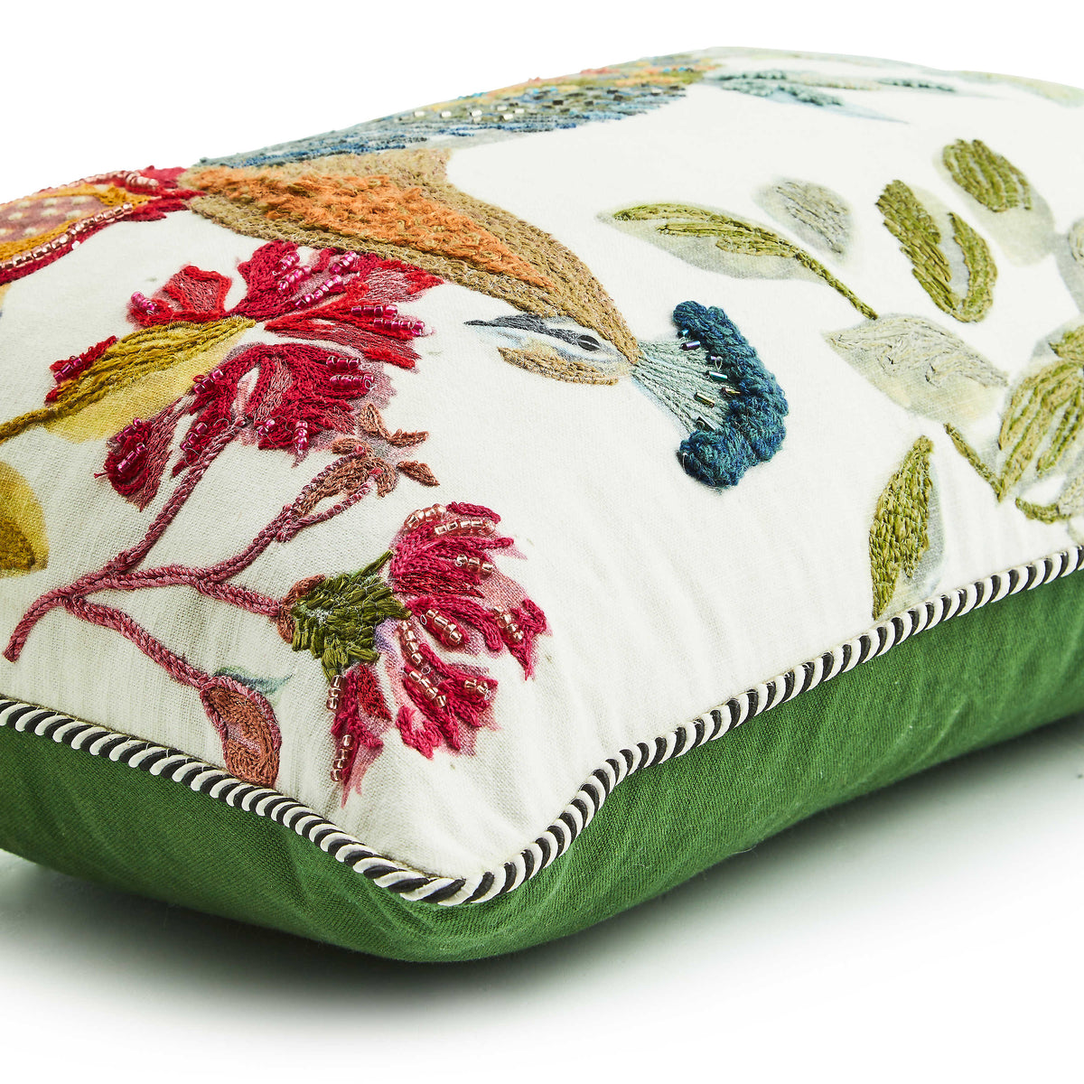 Embroidered lumbar pillow with colorful floral and bird designs, green velvet back, and corded trim.