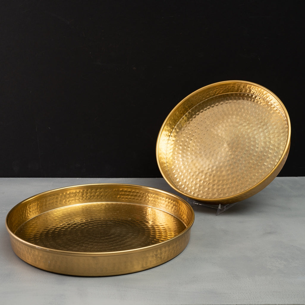 Two round gold aluminum trays with a hammered finish, one flat and one propped up.