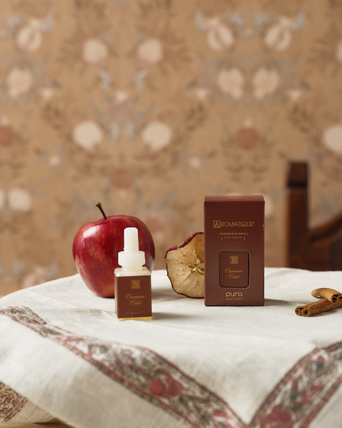 Cinnamon Cider Pura fragrance refill bottle and box on a table with an apple and cinnamon sticks.