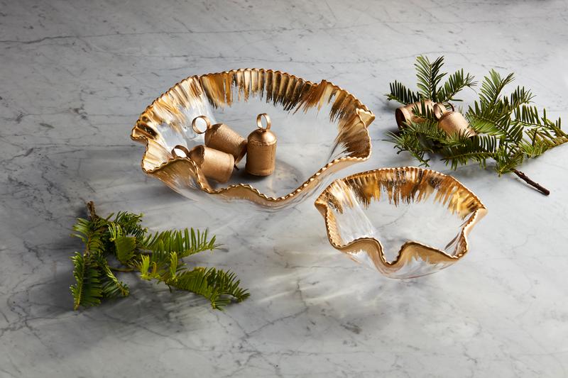 Two clear glass ruffle bowls with hand-painted gold rims on a marble surface with greenery.