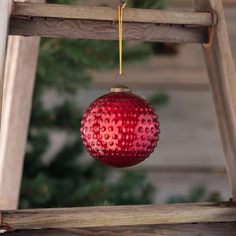 Round 5-inch ruby red mercury glass ornament with a vintage hobnail texture hanging by a gold cord.