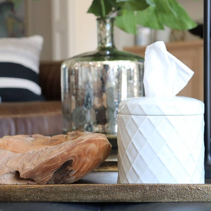 White ceramic diamond-patterned tissue vessel on a tray next to a wooden bowl and glass vase.