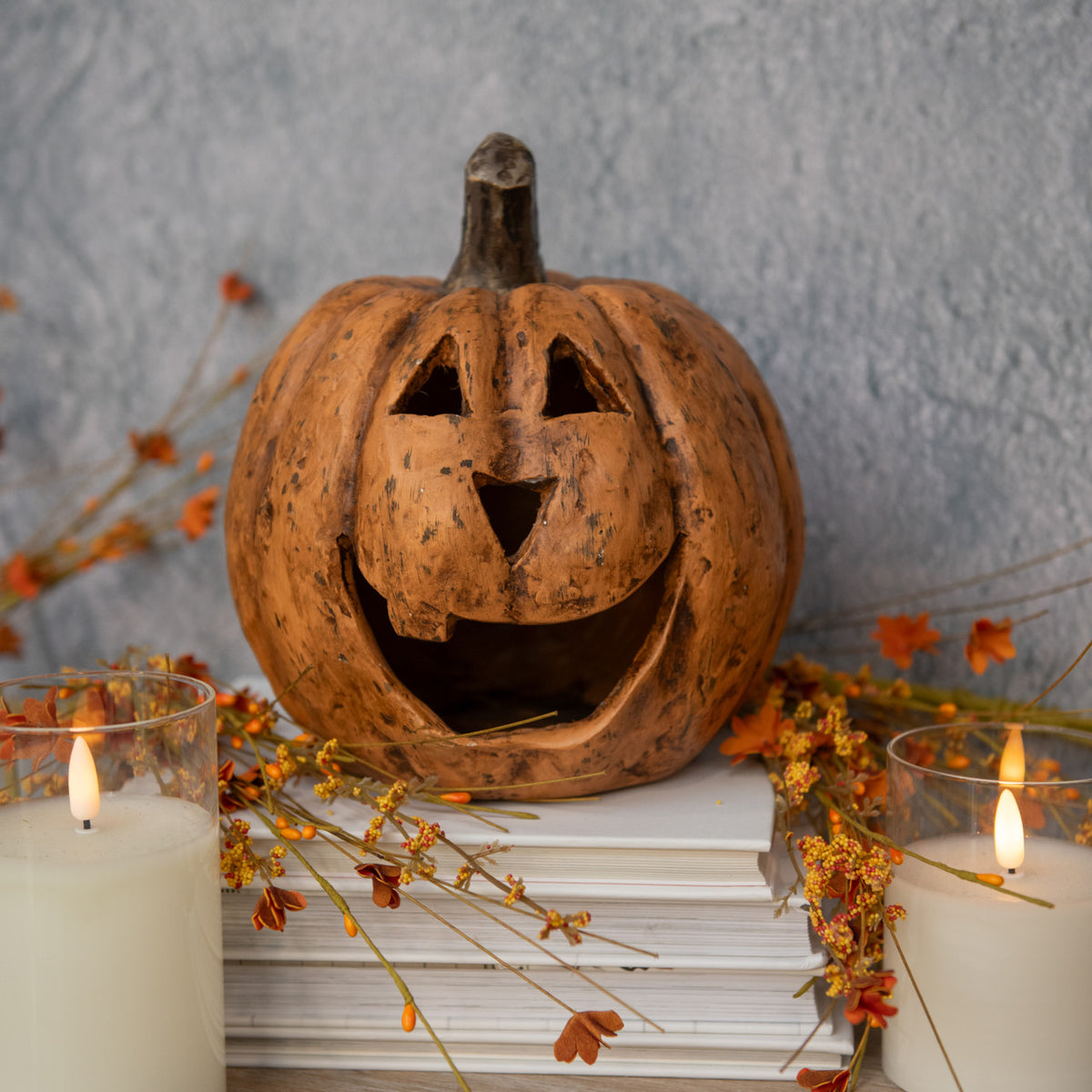 8-inch terracotta big mouth pumpkin jack-o'-lantern on a stack of white books with candles.