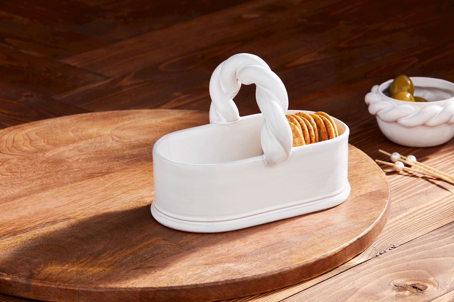 White terracotta Twisted Handle Tidbit basket holding crackers on a wooden serving board.