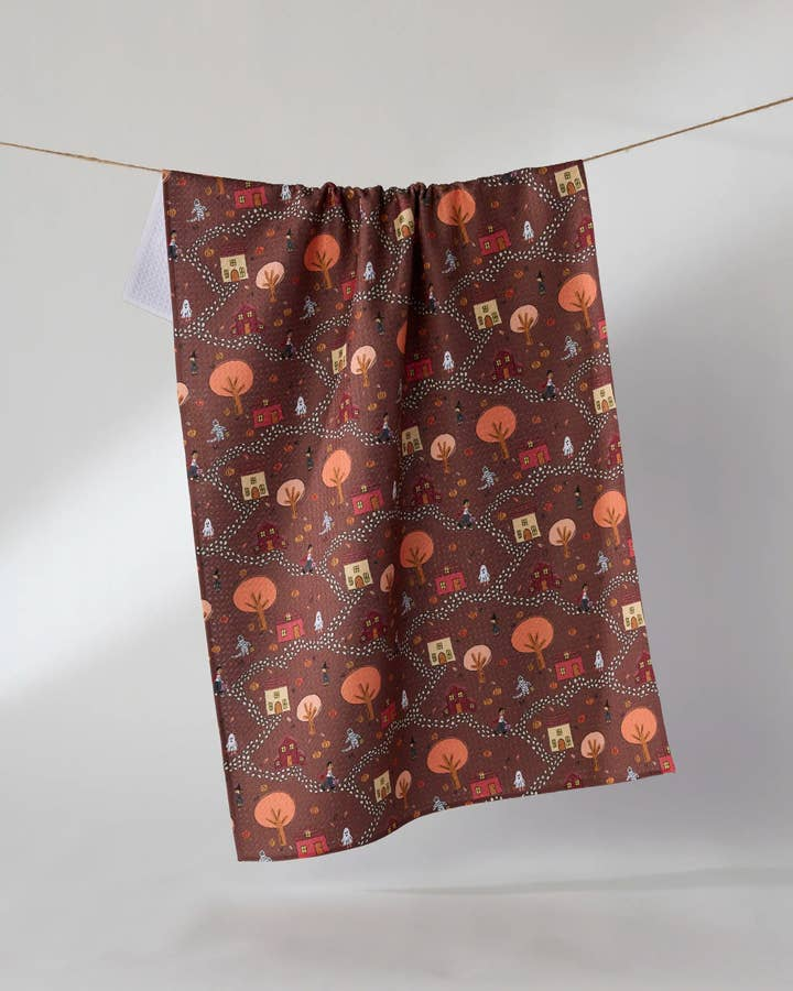 Halloween tea towel with a brown waffle weave pattern featuring houses, trees, and ghosts.