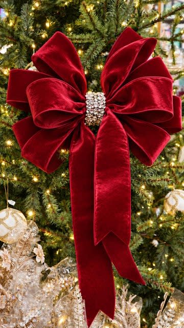 Large red velvet holiday bow with a rhinestone center knot on a decorated Christmas tree.
