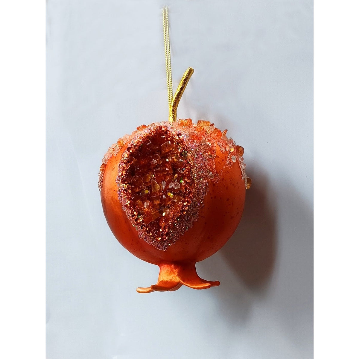 Orange faux pomegranate ornament with a split-open side showing shimmering textured seeds.