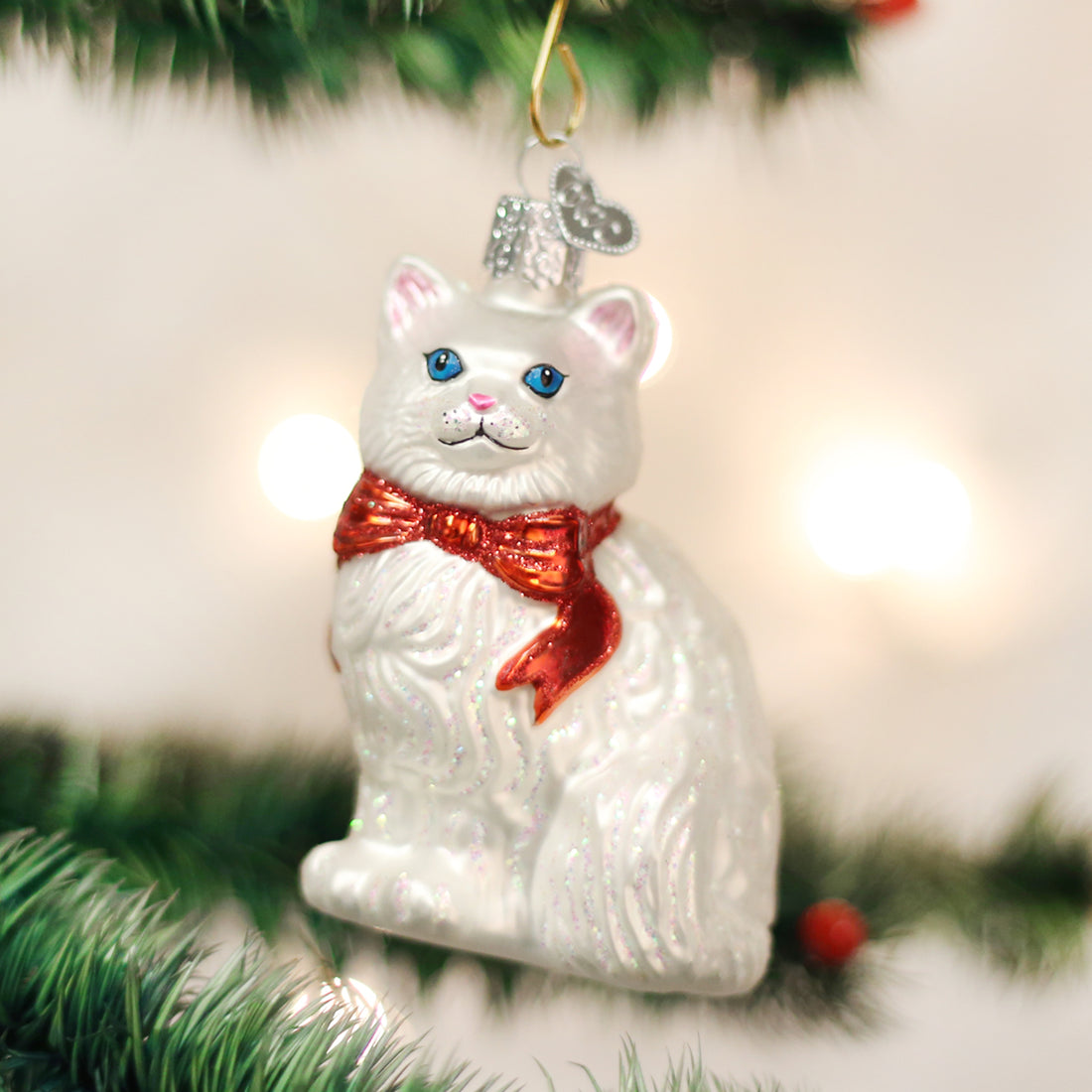 White glass Princess Kitty ornament with a red glitter bow hanging on a Christmas tree branch.