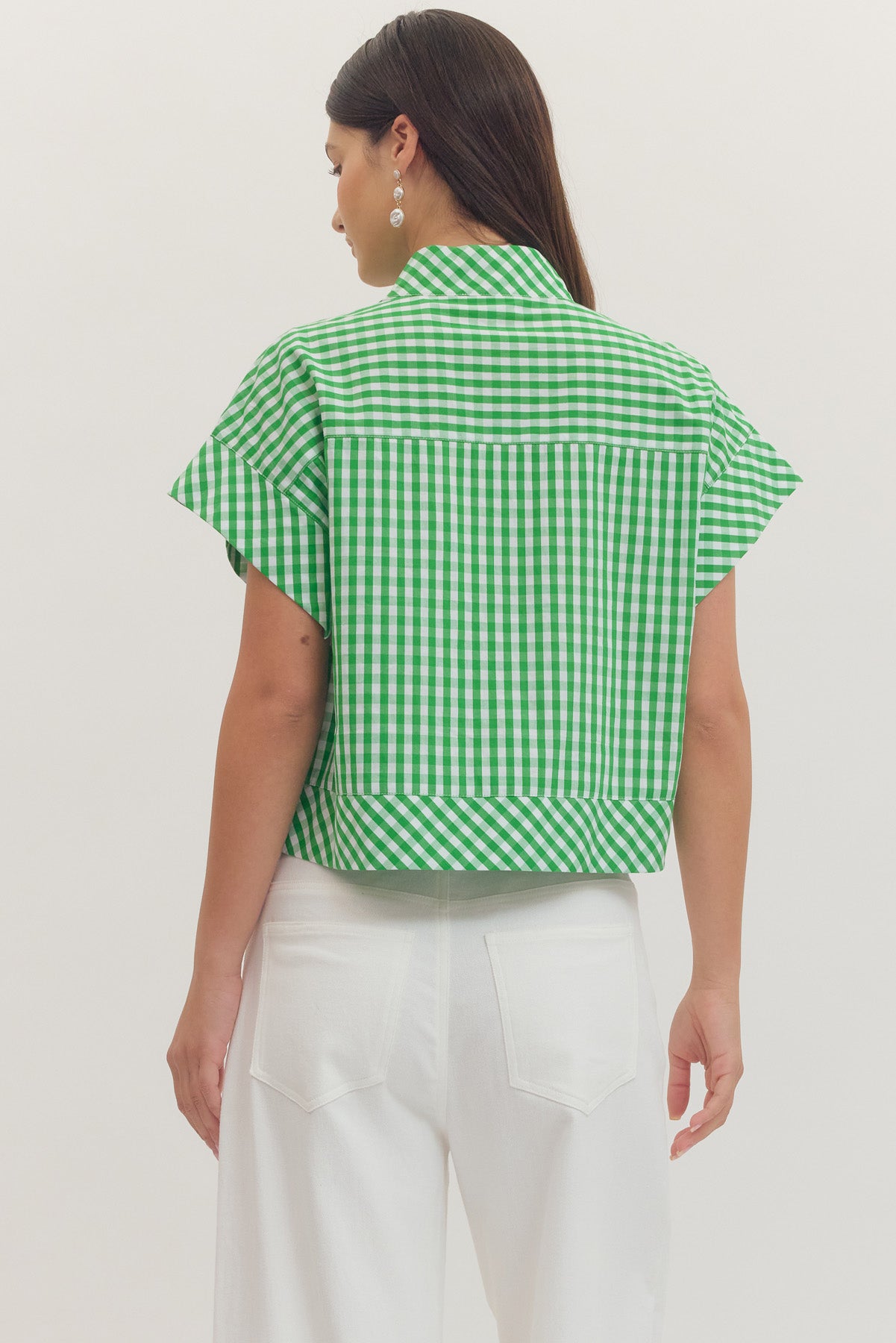 Back view of a woman wearing a green and white gingham print cap sleeve top with white pants.