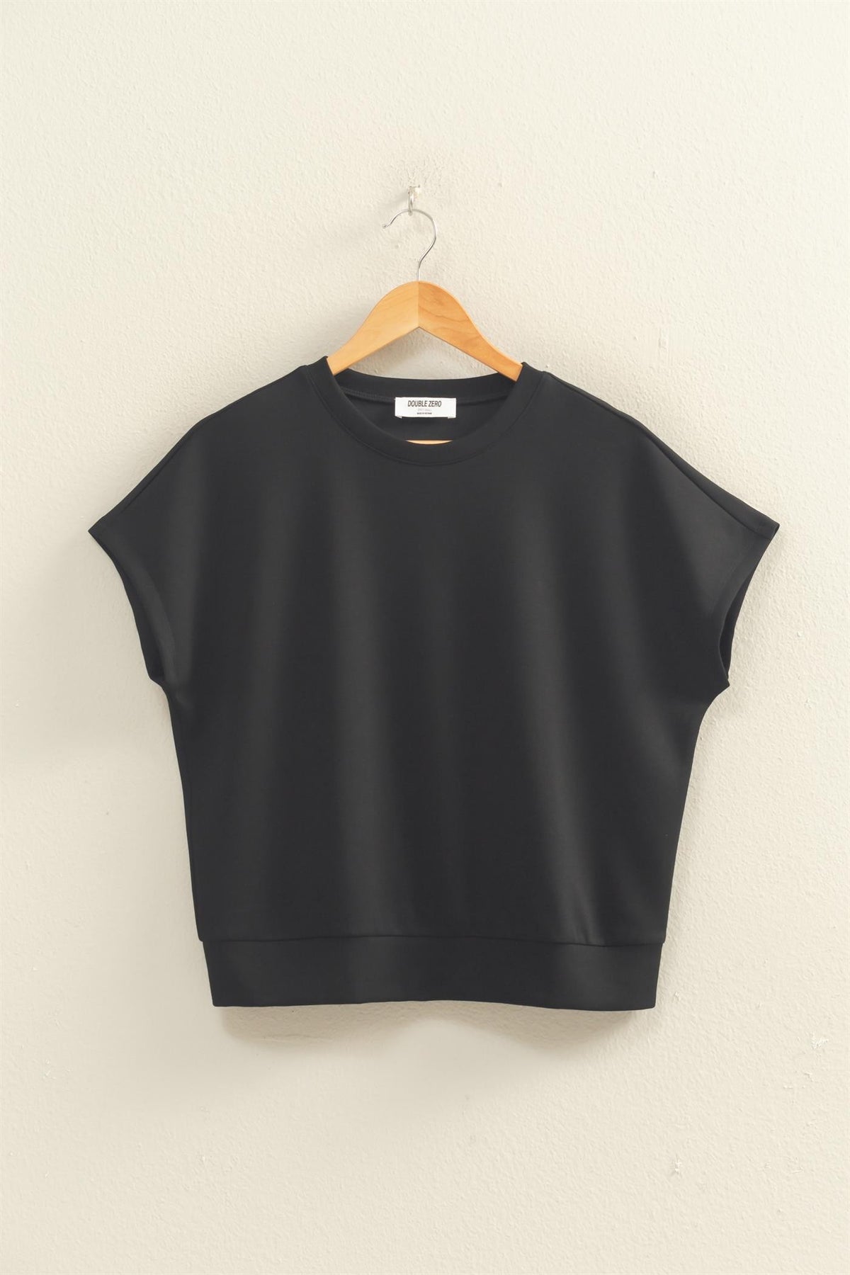 Black Alecia crew neck top with short dolman sleeves hanging on a wooden hanger.