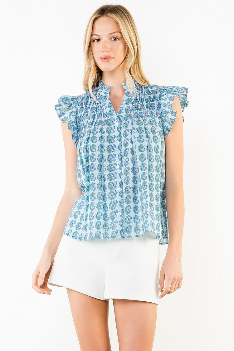 Woman wearing the Natalie Flutter Sleeve Floral Pattern Top in blue with white shorts.