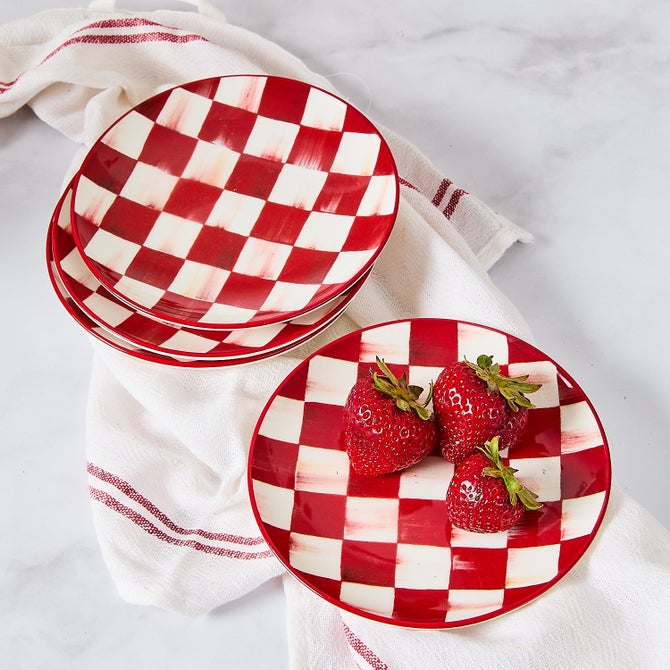 A stack of red and white checkered appetizer plates with three strawberries on the top plate.