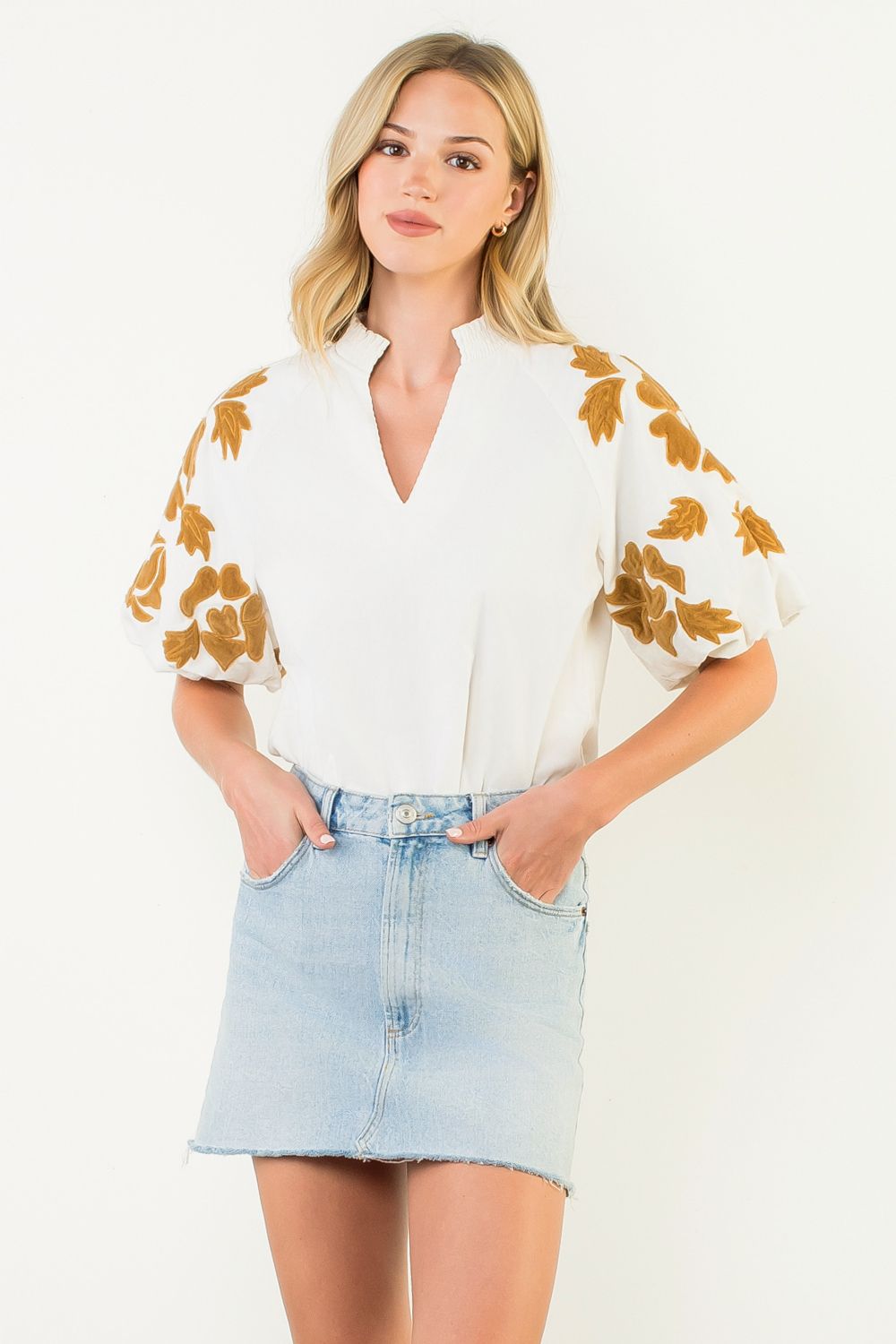 Woman wearing a white Sophia top with gold chenille floral embroidery on puff sleeves.