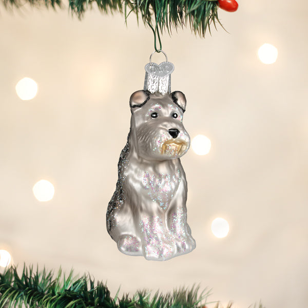 Grey Schnauzer glass ornament with glitter accents hanging on a Christmas tree branch.
