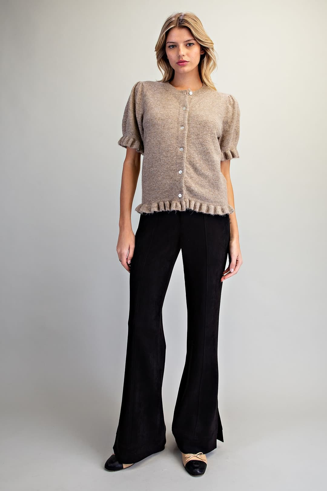 Woman wearing the Ezra Ruffle Trim Short Sleeve Cardigan in tan with black flared trousers.