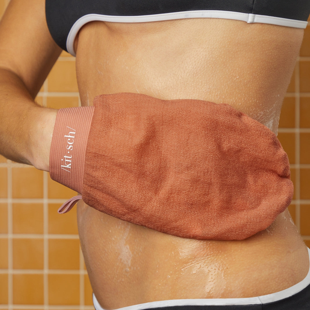 Black exfoliating glove with terracotta accents designed as a body scrubber mitt.