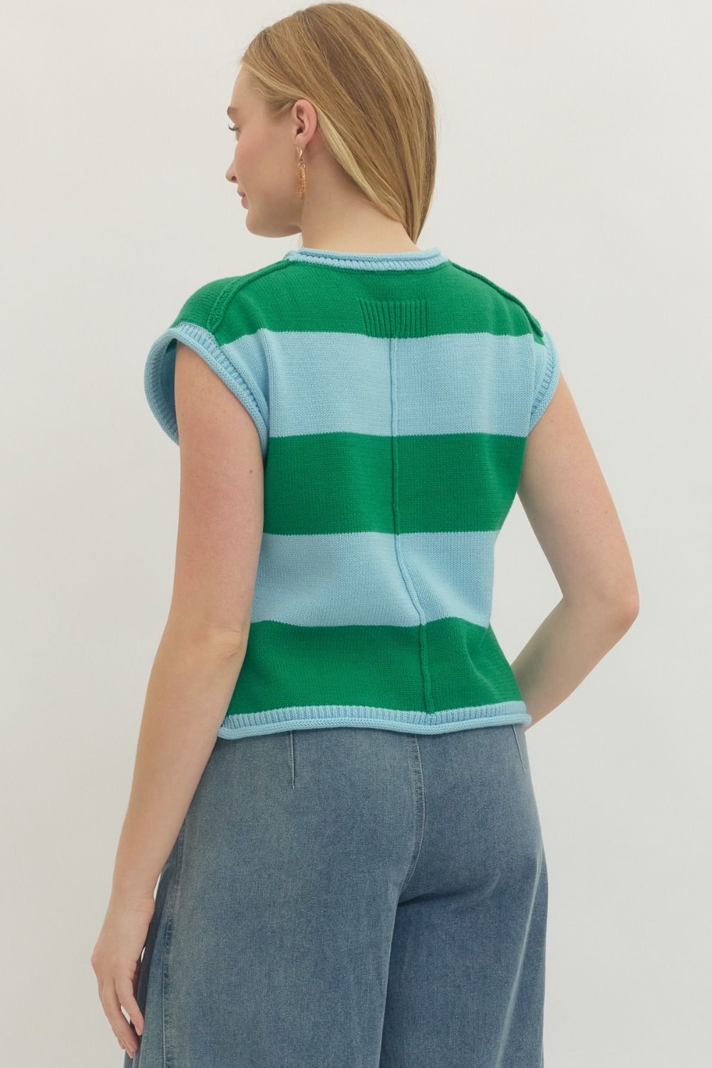 Back view of a woman wearing a green and light blue striped knit cap sleeve top with denim pants.