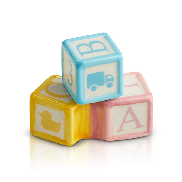 Three ceramic baby blocks in blue, yellow, and pink stacked together with letters and icons.