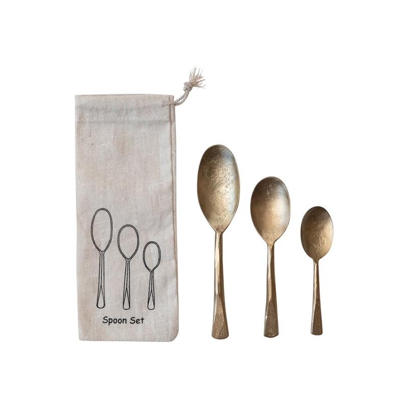 Set of three hand-forged iron spoons in varying sizes next to a linen drawstring storage bag.