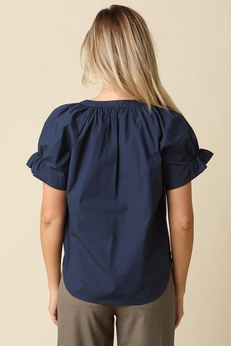 Back view of a woman wearing a navy blue Hylee Ruffle Sleeve Peasant Blouse with olive pants.