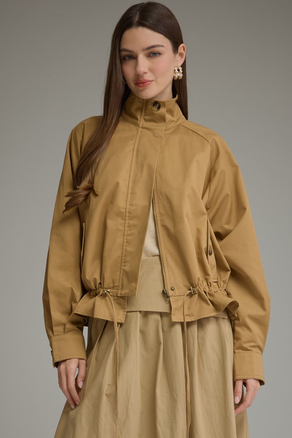 Woman wearing the Andrea Solid Long Sleeve Jacket in tan with a high collar and drawstring hem.
