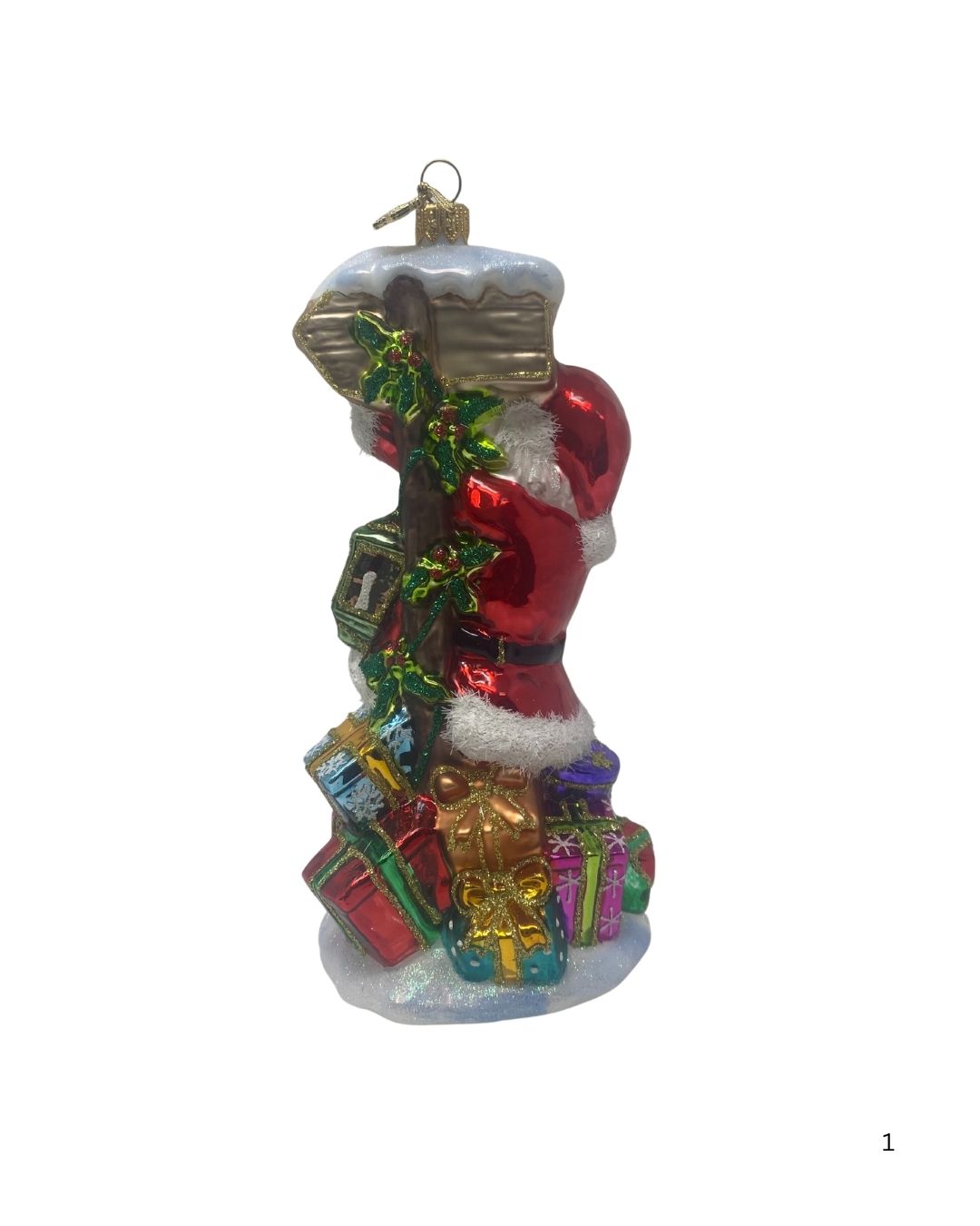Glass Santa ornament climbing a North Pole signpost surrounded by colorful gift boxes.