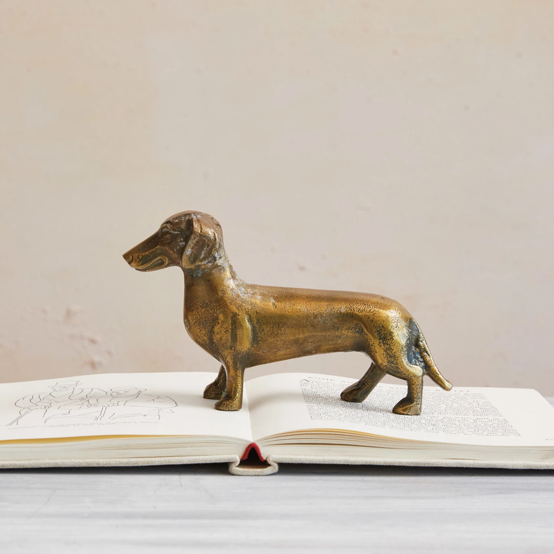 Aluminum dachshund figurine with an antique brass finish standing on an open book.