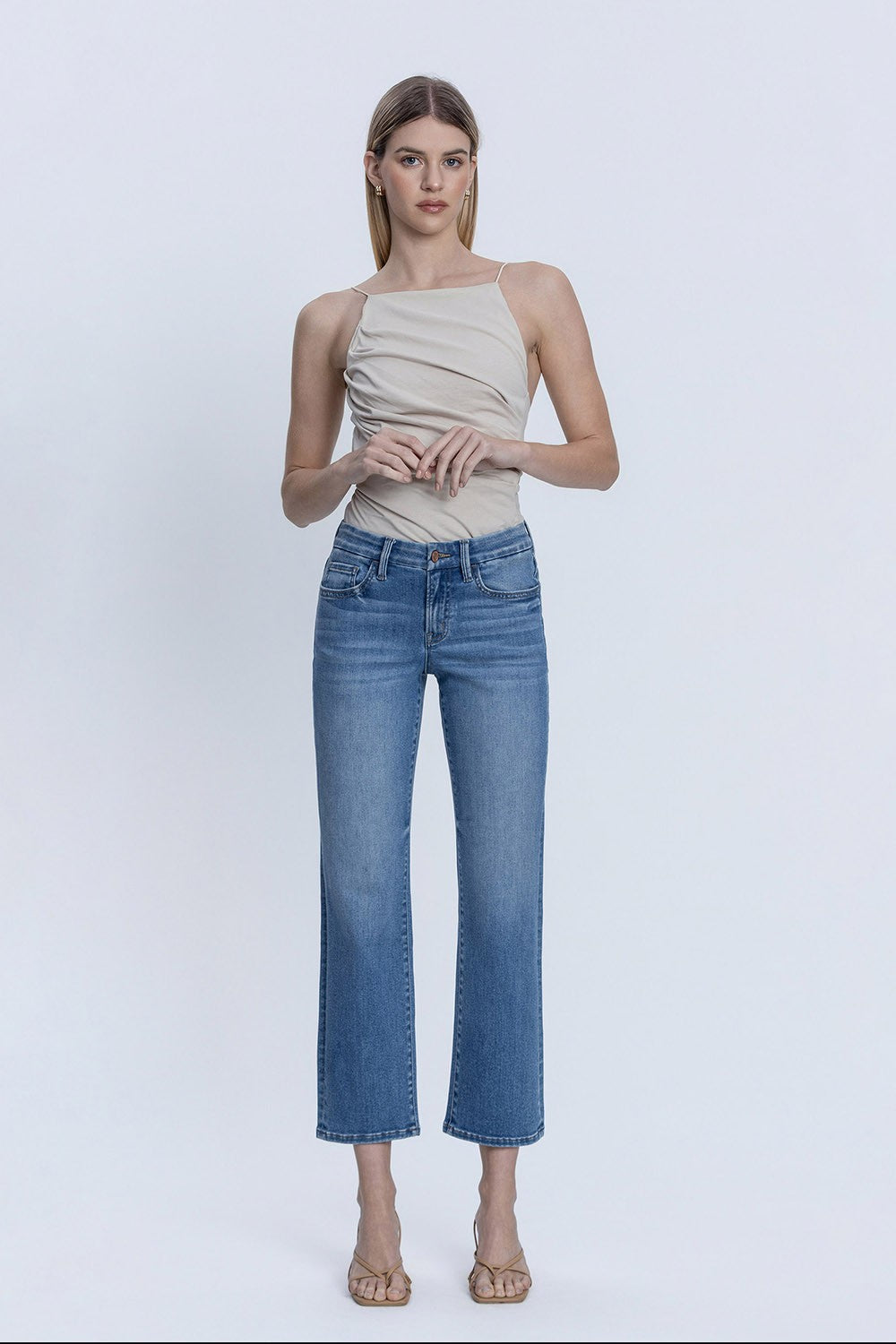 Woman wearing Delilah mid-rise medium dark wash ankle straight jeans with a beige top.