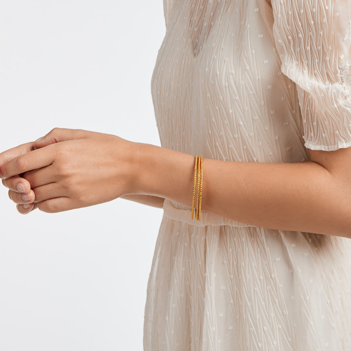 A person wearing three thin, gold-beaded Colette Bead Bangles on their wrist.
